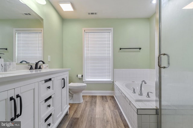 bathroom with wood-type flooring, vanity, tiled bath, and toilet