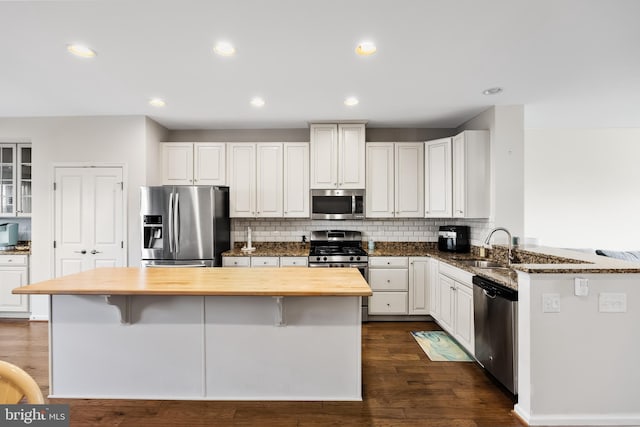 kitchen with white cabinets, dark wood finished floors, wood counters, appliances with stainless steel finishes, and a kitchen breakfast bar