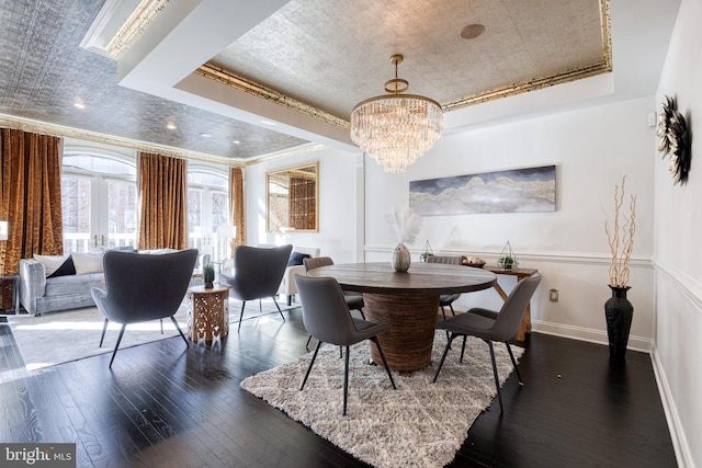 dining area with dark wood-type flooring, crown molding, a raised ceiling, and an inviting chandelier