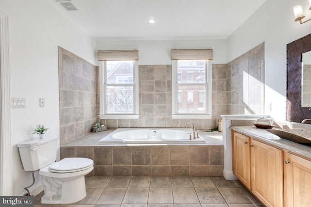 bathroom with a relaxing tiled tub, vanity, tile patterned floors, and toilet