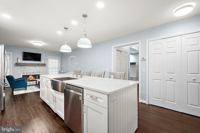 kitchen featuring a kitchen island with sink, sink, decorative light fixtures, white cabinetry, and stainless steel appliances