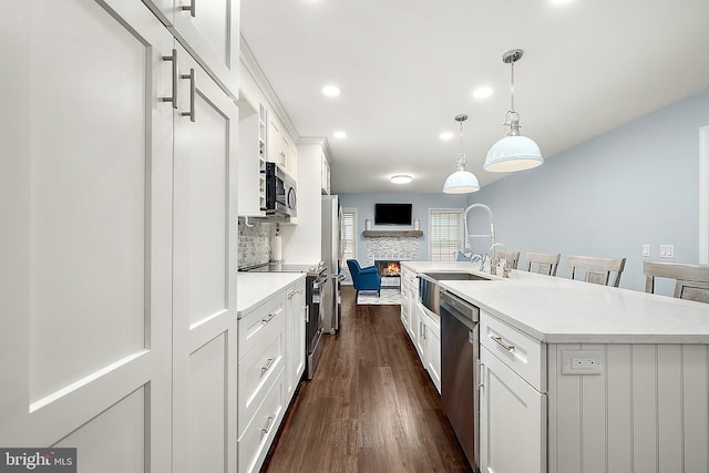 kitchen featuring appliances with stainless steel finishes, a kitchen island with sink, dark wood-type flooring, pendant lighting, and white cabinetry