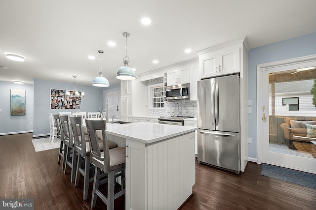 kitchen featuring white cabinetry, hanging light fixtures, dark wood-type flooring, stainless steel appliances, and an island with sink