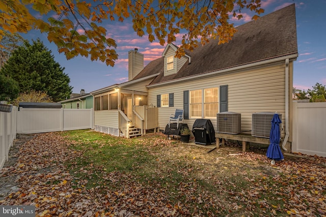 back house at dusk with a sunroom and central AC