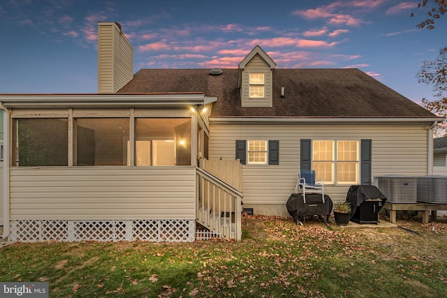 back house at dusk featuring a sunroom and a lawn