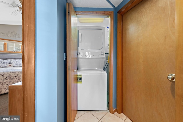 laundry area featuring a textured ceiling, light tile patterned floors, and stacked washer and clothes dryer