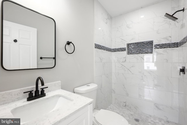 bathroom with a tile shower, vanity, and toilet
