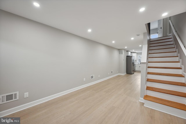 basement with stainless steel fridge and light hardwood / wood-style floors