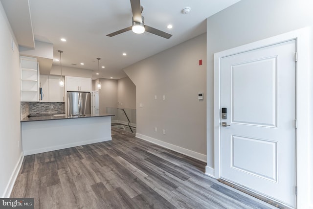 kitchen with kitchen peninsula, stainless steel fridge, dark hardwood / wood-style flooring, white cabinets, and hanging light fixtures