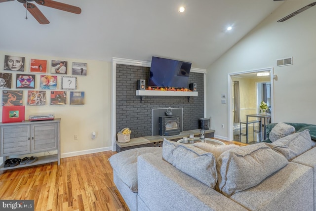 living room featuring high vaulted ceiling, light hardwood / wood-style flooring, a wood stove, and ceiling fan