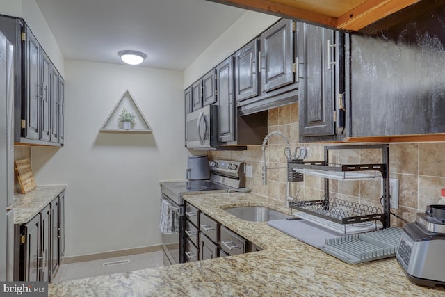 kitchen with light stone countertops, sink, backsplash, light tile patterned floors, and appliances with stainless steel finishes