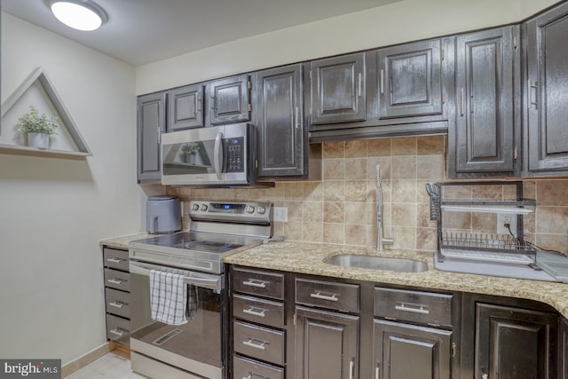 kitchen with decorative backsplash, sink, light stone countertops, and stainless steel appliances