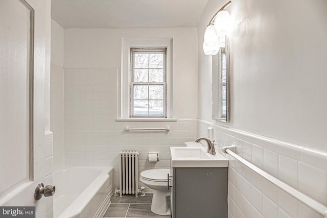 bathroom featuring radiator, vanity, a bath, tile walls, and toilet