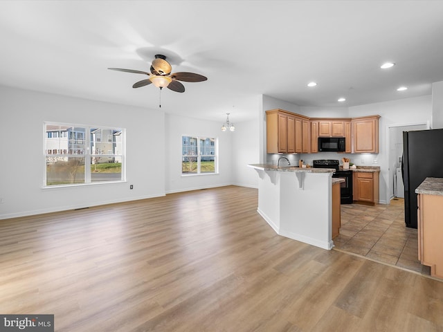 kitchen featuring black appliances, a kitchen breakfast bar, ceiling fan with notable chandelier, sink, and light hardwood / wood-style flooring