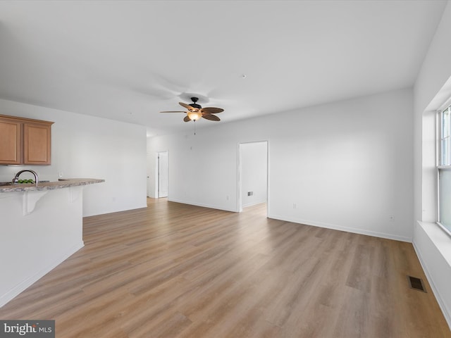 unfurnished living room featuring light hardwood / wood-style flooring, ceiling fan, and sink