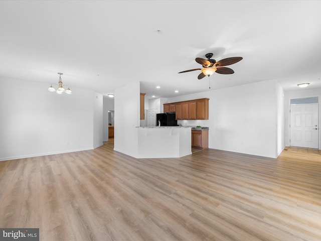 unfurnished living room with ceiling fan with notable chandelier and light hardwood / wood-style flooring