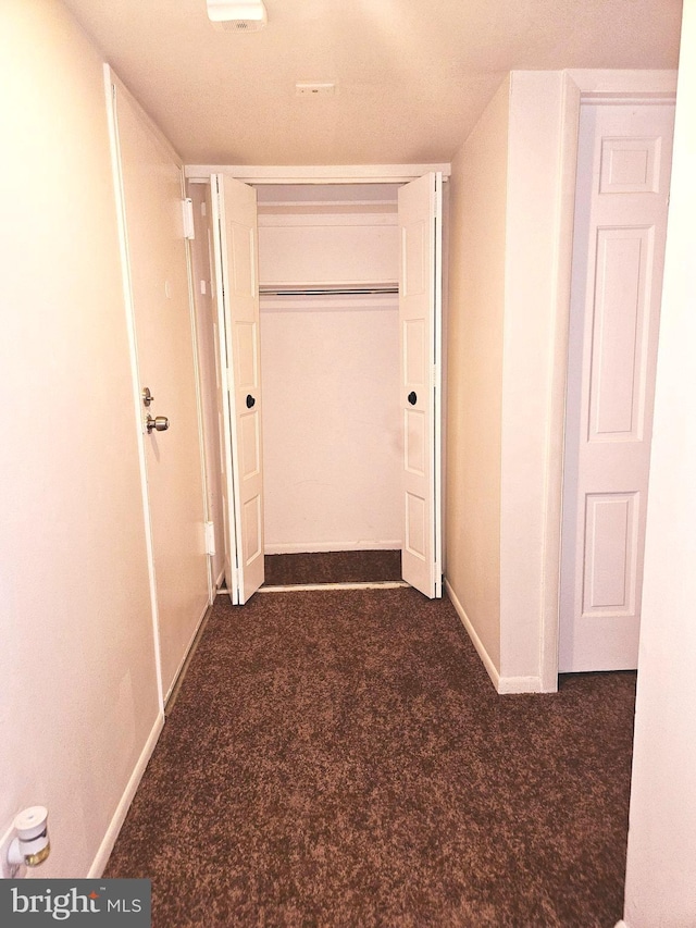 hallway with a textured ceiling and dark colored carpet