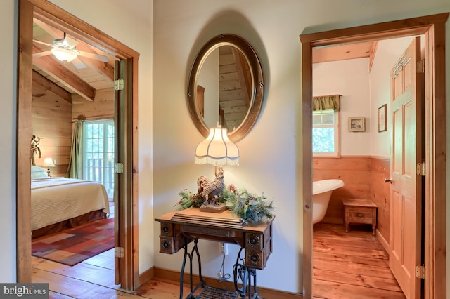 hall with vaulted ceiling with beams, light hardwood / wood-style floors, a healthy amount of sunlight, and wood walls