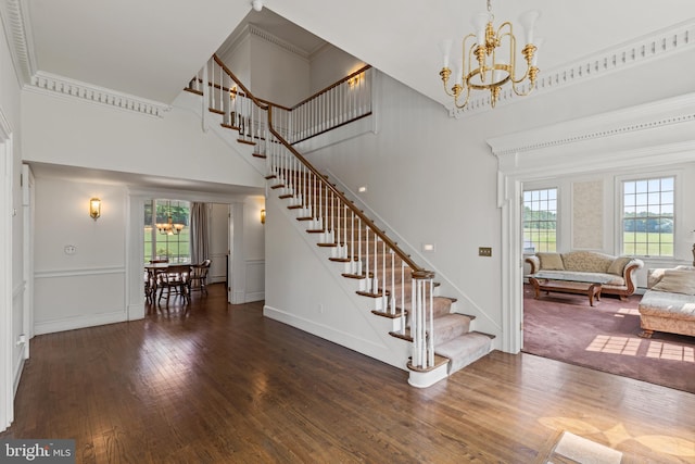 staircase featuring a towering ceiling, hardwood / wood-style flooring, ornamental molding, and a notable chandelier