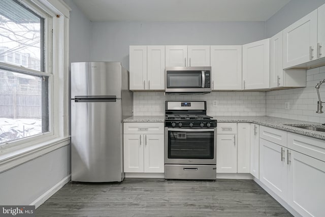 kitchen with white cabinets, hardwood / wood-style flooring, decorative backsplash, and appliances with stainless steel finishes