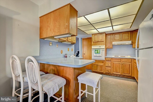 kitchen with a kitchen bar, white appliances, kitchen peninsula, and light colored carpet