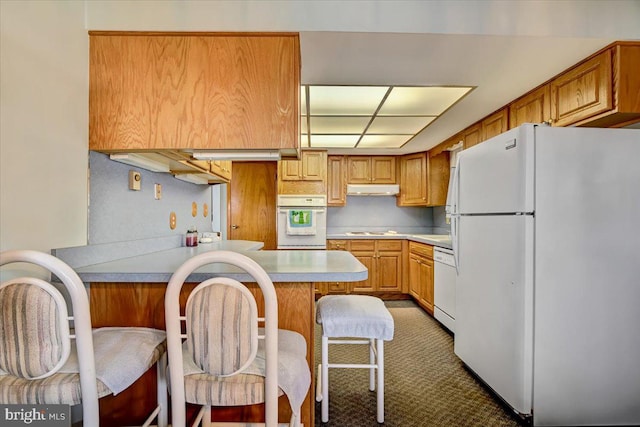 kitchen featuring kitchen peninsula, white appliances, dark colored carpet, and a breakfast bar