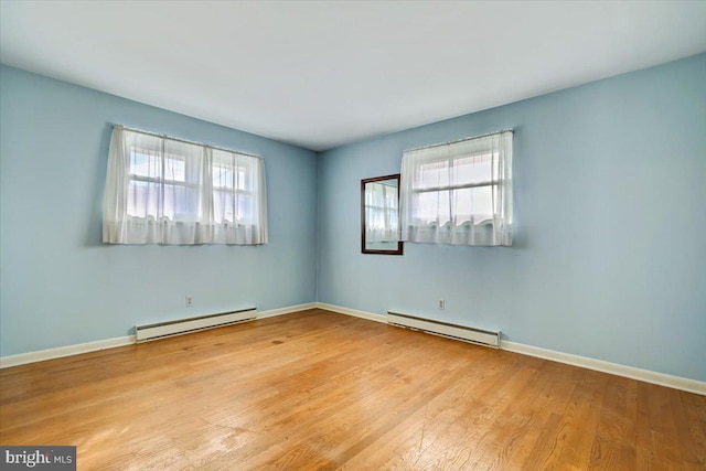 empty room featuring a healthy amount of sunlight, baseboard heating, and light hardwood / wood-style flooring