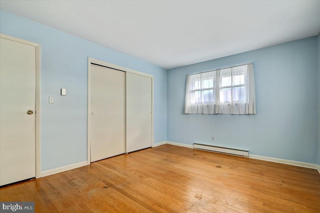 unfurnished bedroom with a closet, light hardwood / wood-style flooring, and a baseboard heating unit