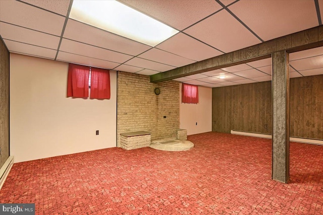 basement featuring a paneled ceiling, a baseboard radiator, and wood walls