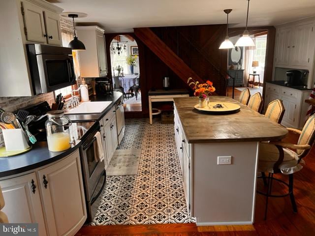 kitchen featuring appliances with stainless steel finishes, decorative light fixtures, white cabinetry, and a kitchen breakfast bar