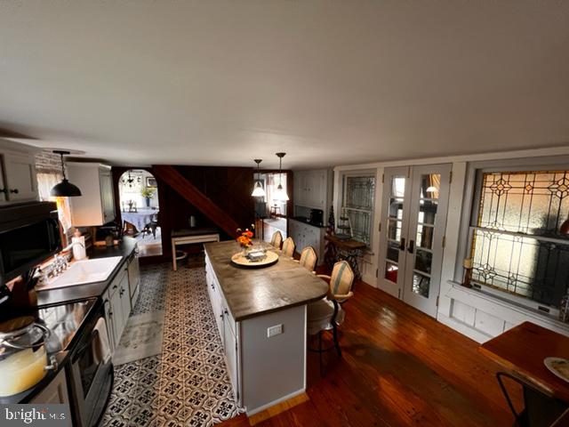 kitchen with french doors, dark wood-type flooring, decorative light fixtures, white cabinets, and a kitchen island