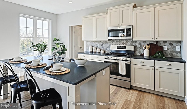 kitchen featuring decorative backsplash, white cabinetry, stainless steel appliances, and light wood-type flooring