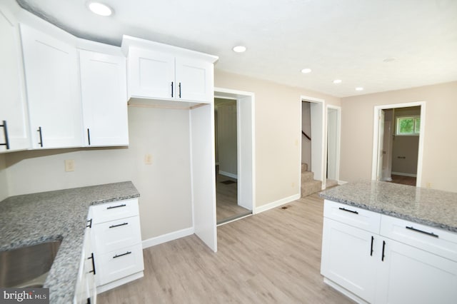 kitchen with light stone countertops, light hardwood / wood-style flooring, and white cabinetry