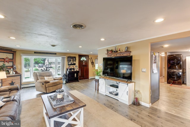 living room with stacked washer / dryer, crown molding, light hardwood / wood-style floors, and a baseboard radiator