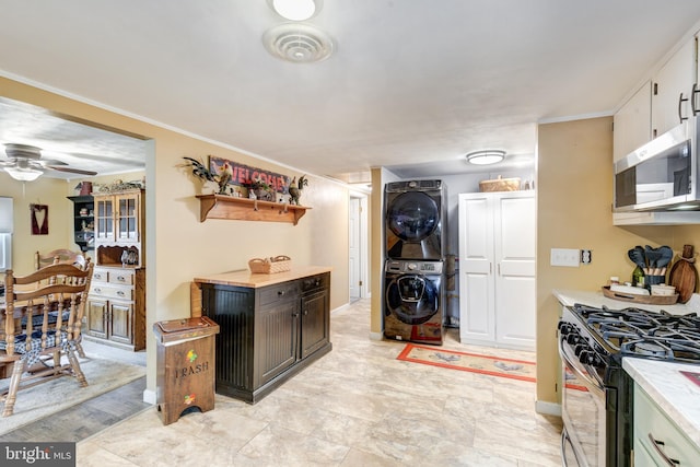 kitchen with ceiling fan, stacked washing maching and dryer, crown molding, range with gas stovetop, and white cabinets