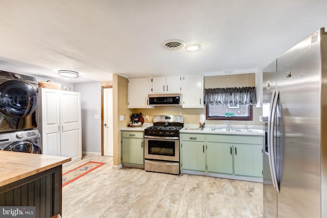 kitchen with stacked washer and clothes dryer, green cabinets, sink, appliances with stainless steel finishes, and white cabinetry