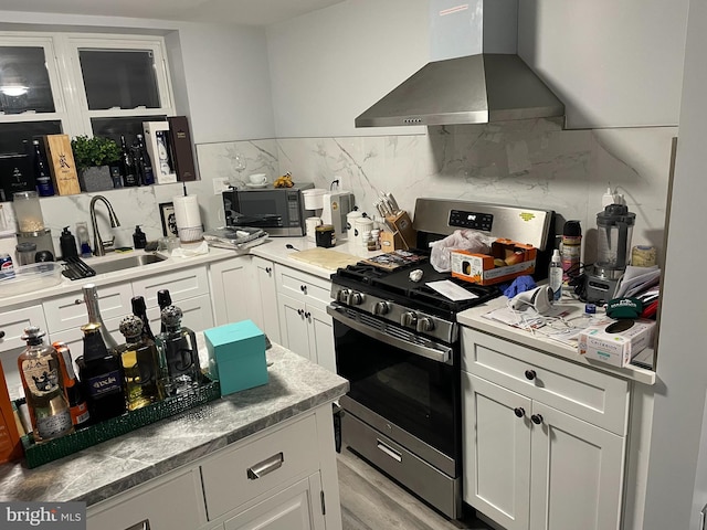 kitchen featuring appliances with stainless steel finishes, light wood-type flooring, sink, wall chimney range hood, and white cabinetry