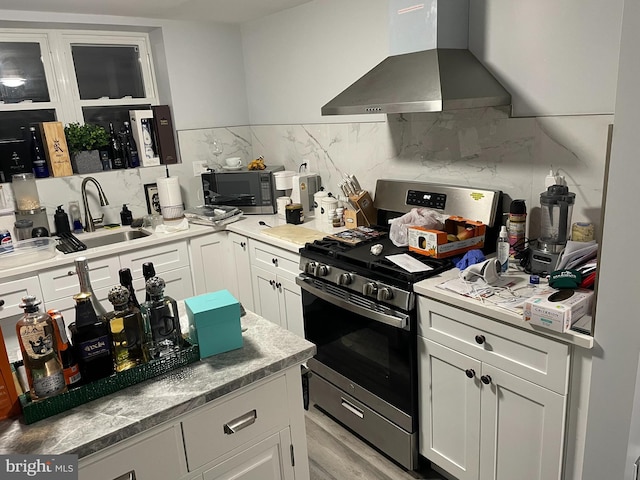 kitchen with stainless steel gas range, white cabinets, black microwave, a sink, and wall chimney exhaust hood