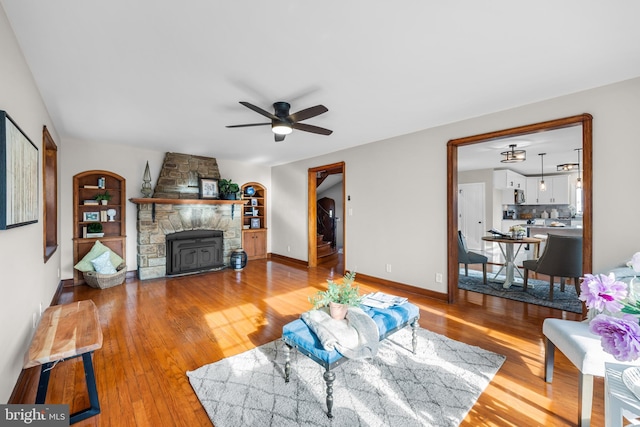 living room with a stone fireplace, ceiling fan, and light hardwood / wood-style floors