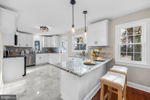 kitchen featuring kitchen peninsula, light stone countertops, pendant lighting, dishwasher, and white cabinetry