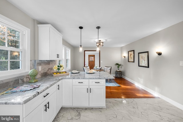 kitchen featuring kitchen peninsula, light stone countertops, white cabinets, and hanging light fixtures