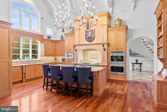 kitchen with backsplash, a towering ceiling, an island with sink, decorative light fixtures, and stainless steel appliances