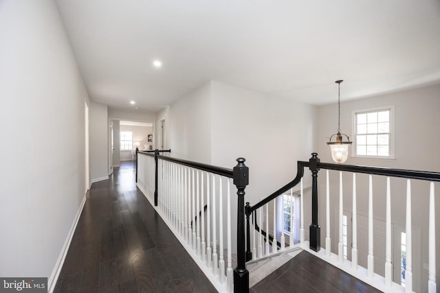 hallway featuring baseboards, wood finished floors, a wealth of natural light, and an upstairs landing