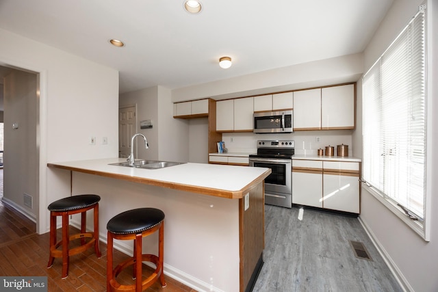 kitchen with stainless steel appliances, sink, light hardwood / wood-style floors, and kitchen peninsula