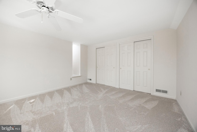 unfurnished bedroom with two closets, ceiling fan, and carpet