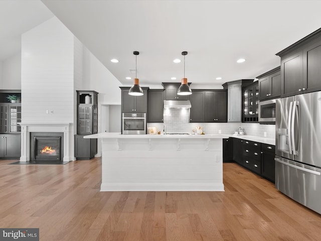 kitchen with stainless steel appliances, pendant lighting, light hardwood / wood-style flooring, a kitchen island, and lofted ceiling