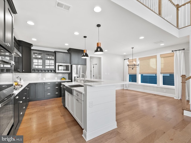 kitchen featuring a center island with sink, stainless steel appliances, decorative light fixtures, and light hardwood / wood-style floors