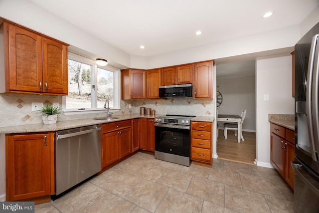 kitchen with brown cabinets, a sink, appliances with stainless steel finishes, decorative backsplash, and light stone countertops