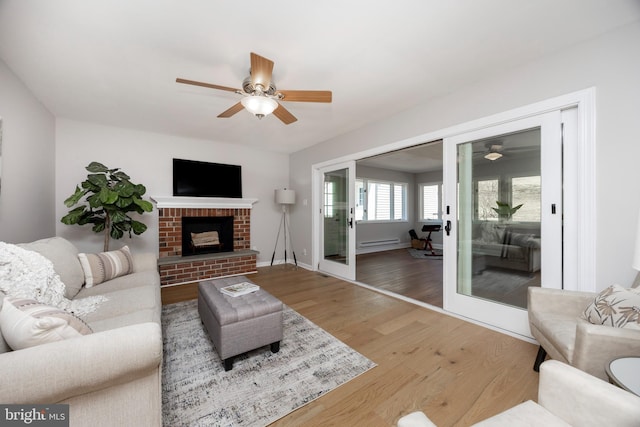 living room with a brick fireplace, baseboards, baseboard heating, wood finished floors, and a ceiling fan