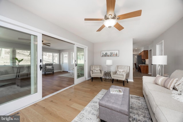 living area featuring a ceiling fan, light wood-type flooring, and baseboards